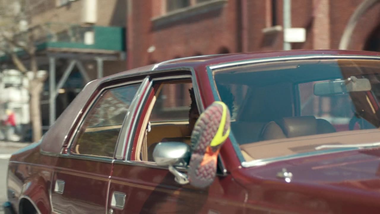 A young man leaning on a vintage car outside New York housing