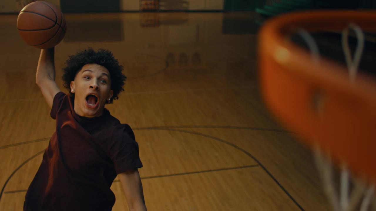 A young player mid-dunk in an empty gym